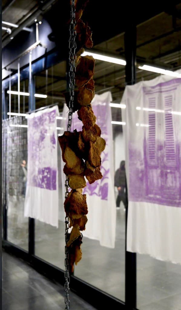 Dried bread-like pieces hanging from a metal chain in a gallery
