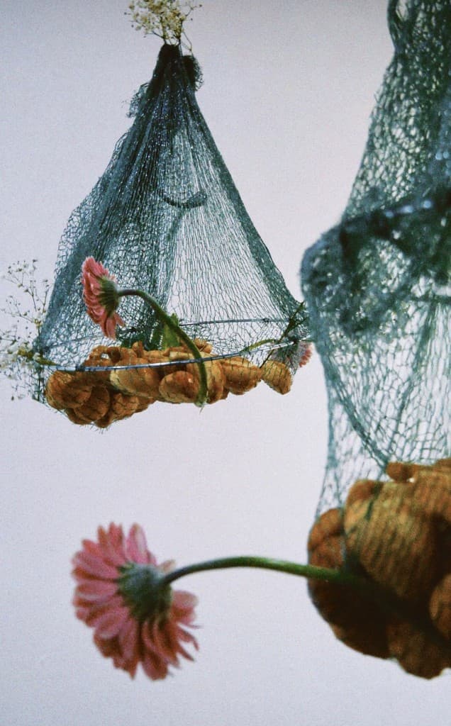 Suspended mesh pods with bread and flowers in a gallery-like space